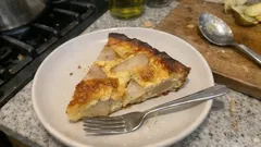 Kawałek domowego ciasta z gruszkami na talerzu, widelczyk, kuchnia w tle