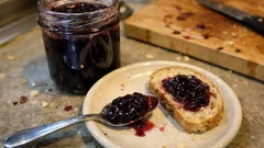 Chleb z dżemem jagodowym na talerzu, słoik dżemu i łyżka na blacie kuchennym