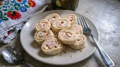 Tortilla z łososiem i serkiem na talerzu, obok widelec na szarym tle, domowy posiłek