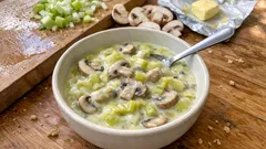 Zupa krem z pieczarek, pora i masła w misce na drewnianym stole, świeże warzywa w tle