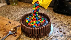 Tort czekoladowy ozdobiony batonikami i kolorowymi cukierkami M&M's na kuchennym blacie.