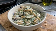 Małże w sosie śmietanowym z pietruszką w białej misce na drewnianej desce