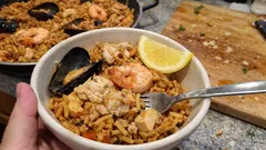 Hiszpańska paella z owocami morza, krewetkami i cytryną w misce, domowe danie na stole.