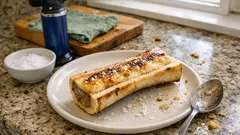 Pieczony szpik kostny na talerzu, obok sól i łyżka, kuchenne tło.