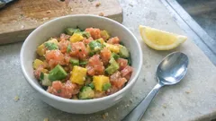 Sałatka z awokado, mango i łososiem w misce, obok łyżka i kawałek cytryny