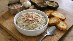 Pasta z tuńczyka w misce, grzanki, bakłażan i czosnek na drewnianej desce