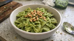 Makaron z pesto bazyliowym i orzeszkami piniowymi w białej misce na kuchennym blacie