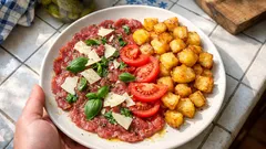 Carpaccio wołowe z parmezanem, pomidorem i pieczonymi ziemniakami na białym talerzu