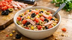 Sałatka z makaronem, szynką, oliwkami, kukurydzą i pomidorami w misce na drewnianym stole.