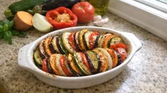 Ratatouille warzywne w naczyniu żaroodpornym na blacie kuchennym, świeże warzywa w tle