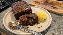 Kawałek ciasta czekoladowego z lodami na talerzu, łyżka obok, stół kuchenny.