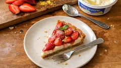 Sernik na zimno z truskawkami na talerzu, widoczne świeże truskawki i serek na stole.