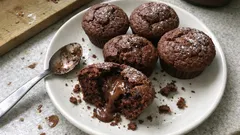 Czekoladowe muffiny z płynnym nadzieniem na białym talerzu, posypane cukrem pudrem.