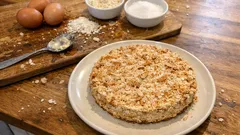 Domowe ciasto orzechowe na talerzu, składniki ciasta i jajka na drewnianej desce.