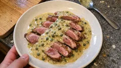 Kaczka w kremowym sosie z kaparami na białym talerzu, danie obiadowe na stole