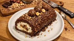 Rolada czekoladowa z kremem, orzechami laskowymi i pralinkami na białym talerzu.