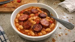 Fasolka po bretońsku z kiełbasą w misce, łyżka, danie na stole kuchennym