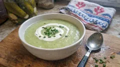 Zupa krem z cukinii z jogurtem i szczypiorkiem w białej misce na drewnianej desce