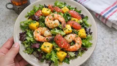 Sałatka z krewetkami, mango i grejpfrutem na liściach zielonej sałaty na talerzu.