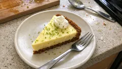 Kawałek tarty cytrynowej z bitą śmietaną na białym talerzu, widelczyk obok deseru