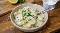 Sałatka ziemniaczana z jogurtem, szczypiorkiem i koperkiem w misce na drewnianym stole