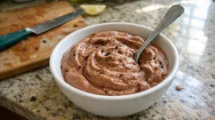 Deser czekoladowy w misce na blacie kuchennym, łyżka w środku, na tle deski z nożem.