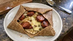 Galette bretońska z kiełbasą i serem na białym talerzu, kuchnia francuska