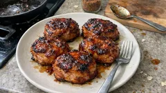 Grillowane kotlety mielone na talerzu, obok widelec i łyżka na desce kuchennej.