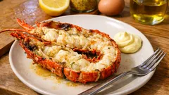 Pieczony homar z masłem czosnkowym i majonezem na talerzu, cytryna w tle