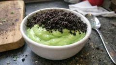 Deser z budyniem pistacjowym i pokruszonymi ciastkami Oreo w białej misce na blacie kuchennym.