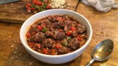 Gulasz wołowy z papryką i pomidorami w białej misce, na drewnianym stole.