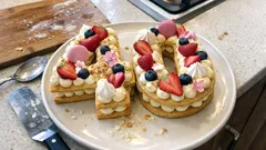 Tort urodzinowy w kształcie liczby 40 z owocami i kremem na talerzu w kuchni.