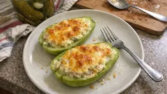 Faszerowana cukinia zapiekana z serem na talerzu, widelcem i dodatkiem ogórków w słoiku