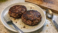 Dwa kotlety mielone na talerzu, widelcem i łyżką na blacie kuchennym