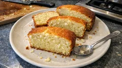 Kawałki domowego ciasta jogurtowego na białym talerzu z łyżeczką, kuchenny blat.