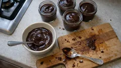 Domowy budyń czekoladowy w miseczkach, deska i łyżki na kuchennym blacie.