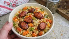 Kuskus z warzywami i grillowaną kiełbasą w misce, domowy obiad na stole kuchennym.