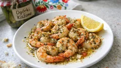 Krewetki smażone z przyprawami na talerzu z cytryną, obok słoik ogórków kiszonych.