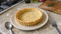 Upieczony spód do tarty na talerzu na blacie kuchennym, obok widelec i łyżka