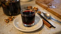 Nalewka orzechowa w szklance na spodku, z laską cynamonu i wanilią na stole.