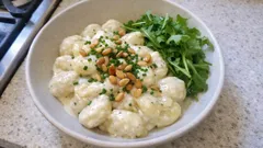 Gnocchi w białym sosie z orzechami i szczypiorkiem, podane z rukolą na talerzu.