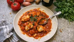 Gulasz z dorsza w sosie pomidorowym na talerzu, zioła i składniki w tle, kuchnia śródziemnomorska.