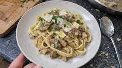 Talerz makaronu tagliatelle z grzybami, parmezanem i natką pietruszki na granitowym blacie.