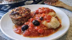 Danie obiadowe z klopsikiem, kluskami i sosem pomidorowym z oliwkami na białym talerzu