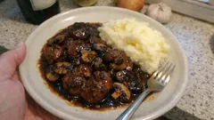 Gulasz wołowy z grzybami i ziemniaczanym puree na talerzu, na tle kuchni.