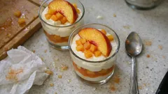 Deser w szklankach z brzoskwiniami i bitą śmietaną na blacie kuchennym.