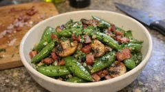 Sałatka z groszkiem cukrowym, boczkiem i pieczarkami w misce na kuchennym blacie.