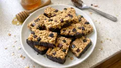 Batoniki musli z czekoladą i suszonymi owocami na talerzu na białym blacie kuchennym.