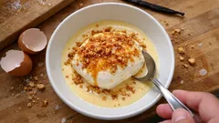 Deser île flottante z kremem waniliowym i prażonymi orzechami, jajka na tle drewnianym.