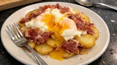 Smażone ziemniaki z jajkiem sadzonym i szynką na białym talerzu, domowe śniadanie